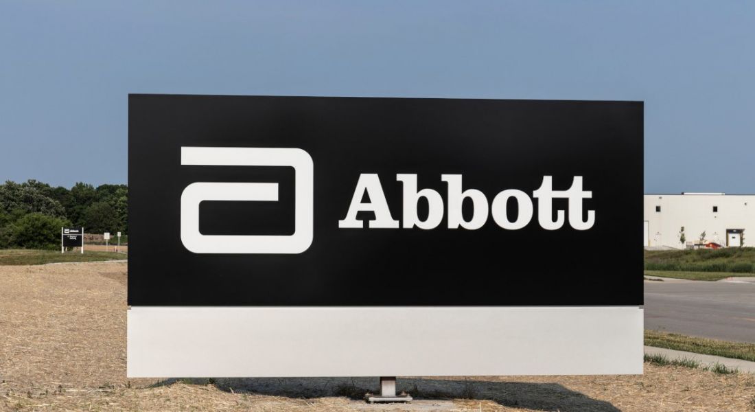 A black board with the Abbott Laboratories logo, pictured against a clear sky next to a road leading to a large building.
