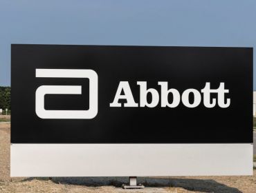 A black board with the Abbott Laboratories logo, pictured against a clear sky next to a road leading to a large building.