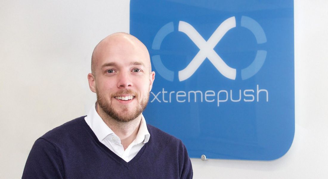 Kevin Collins sits in front of a sign with the Xtremepush logo on it.