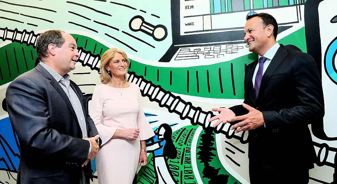 A man and a woman stand on the left talking to Leo Varadkar against a colourful wall.