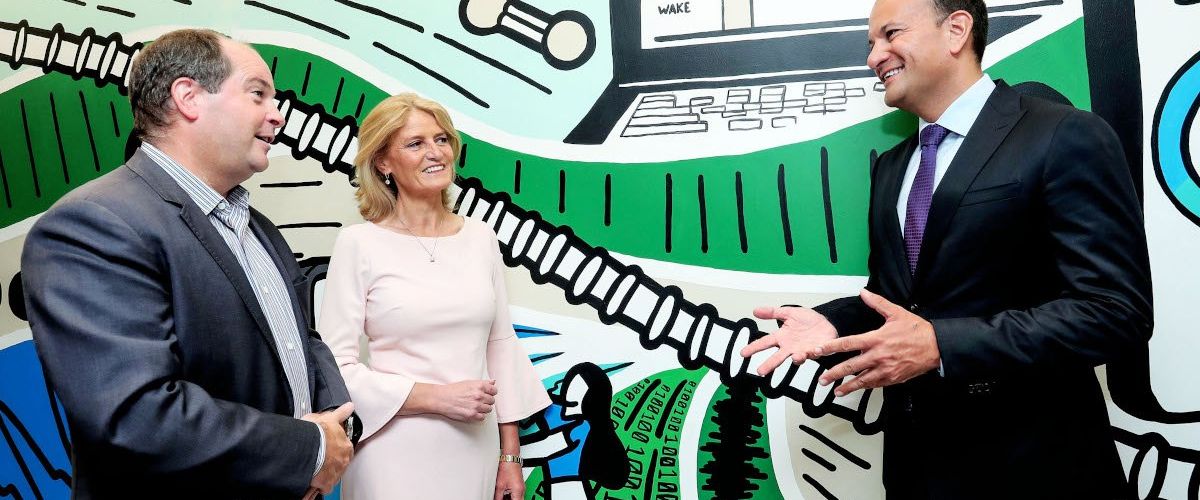 A man and a woman stand on the left talking to Leo Varadkar against a colourful wall.