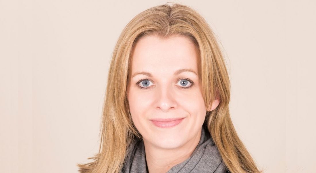 A headshot of Sinead Grogan from Deloitte smiling at the camera against a light beige background.