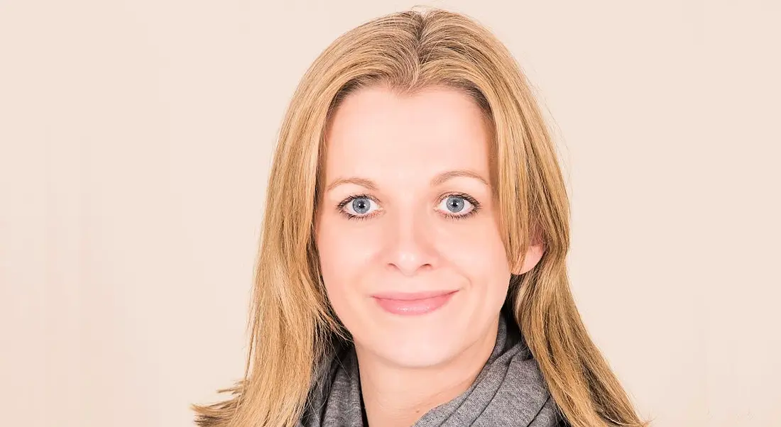 A headshot of Sinead Grogan from Deloitte smiling at the camera against a light beige background.