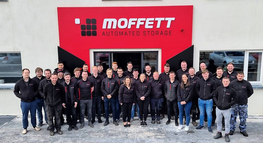 The team at Moffett Automated Storage standing outside in front of the company's sign on a grey building.