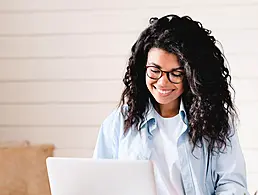 A young woman wearing a yellow t-shirt typing on a laptop. She is working on her software development CV.