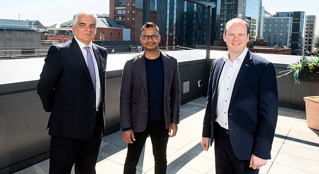 Three men standing next to each other with the Belfast skyline visible behind them.