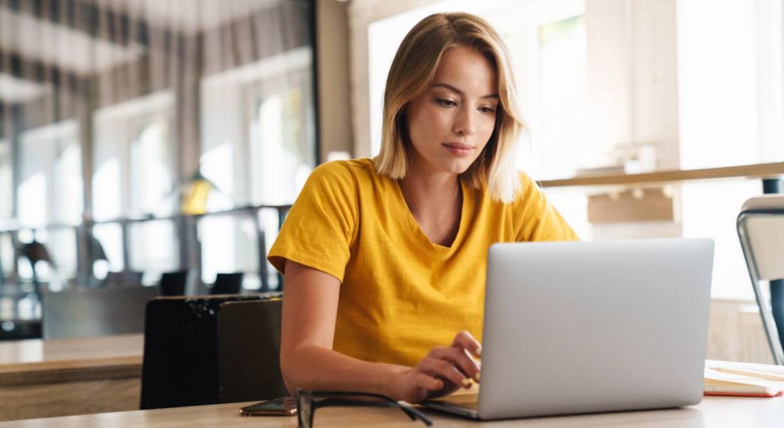 A young woman wearing a yellow t-shirt typing on a laptop. She is working on her software development CV.
