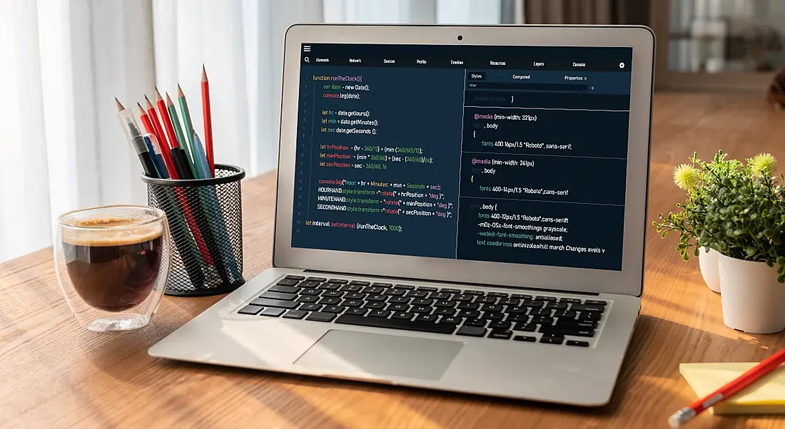 A laptop on a desk surrounded by tiny potted plants, stationery and coffee. There is code on the screen, symbolising SQL skills.