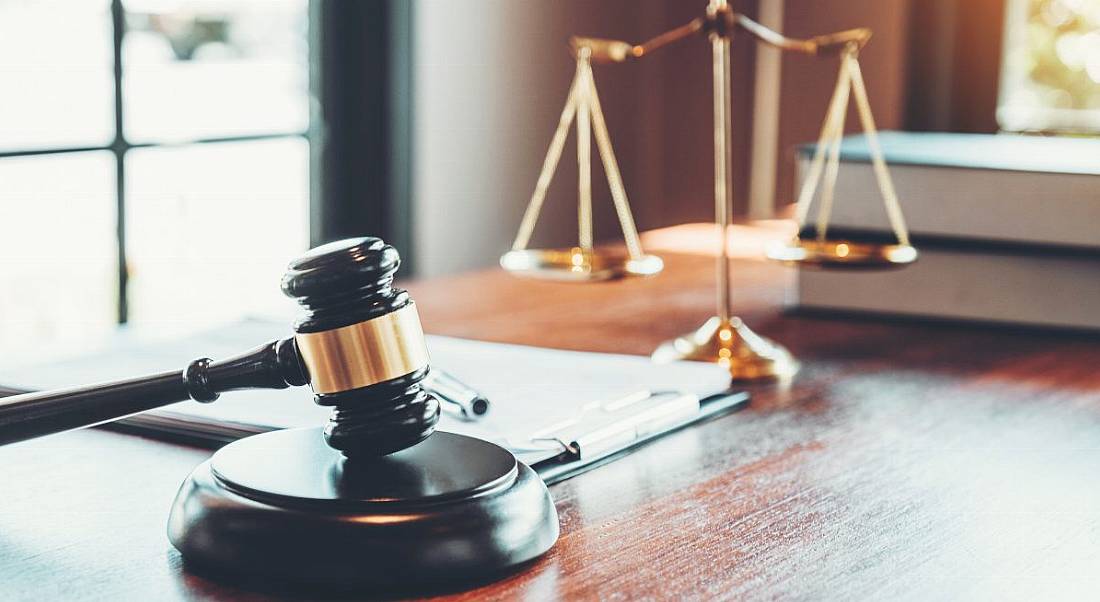 A judge’s gavel resting on the table. IN the background is the scales of justice, symbolising legal issues.