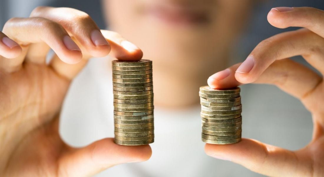 A person holding up two stacks of coins, one is smaller than the other, symbolising a gender pay gap.