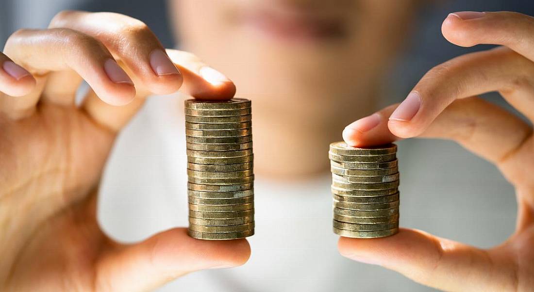 A person holding up two stacks of coins, one is smaller than the other, symbolising a gender pay gap.