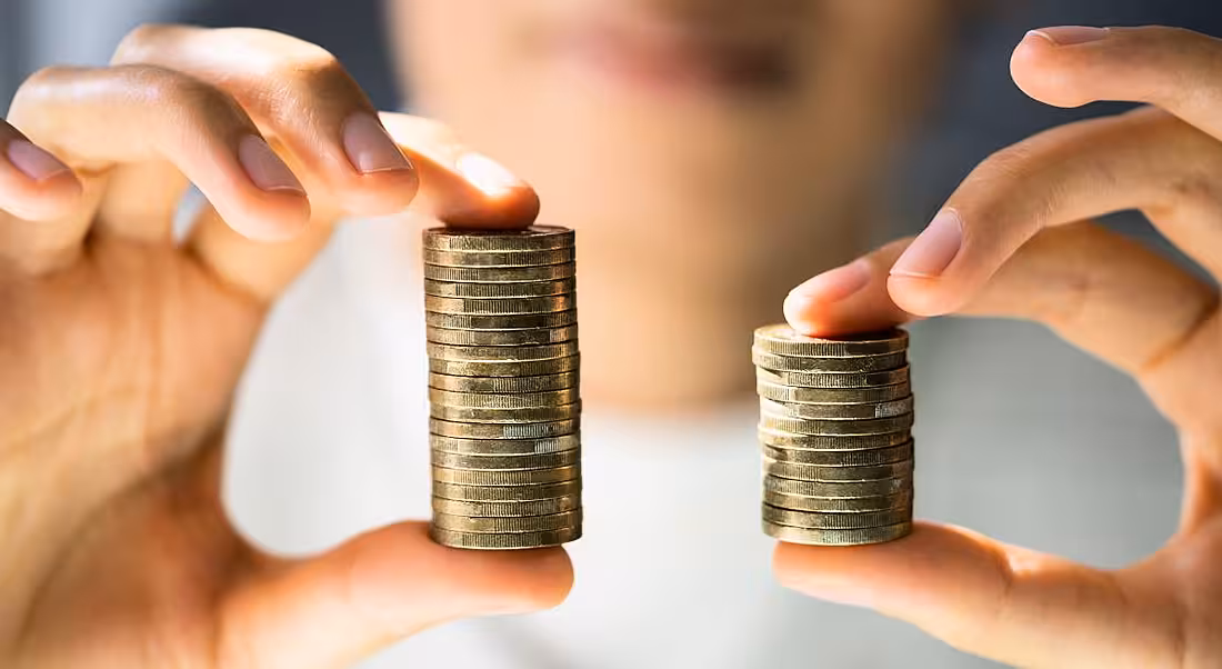 A person holding up two stacks of coins, one is smaller than the other, symbolising a gender pay gap.