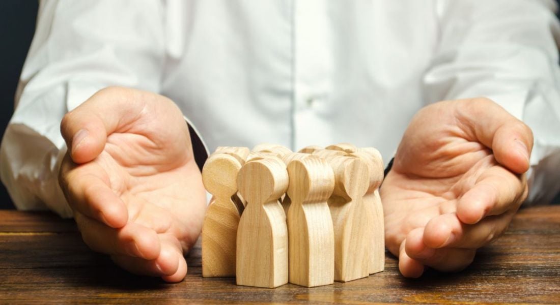 A pair of hands open on a table. In between them is a group of wooden figurines. This symbolises retaining talent.