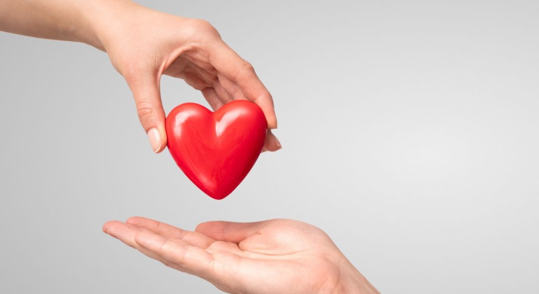 A hand holding a 3D red heart and placing it another open hand, representing a supportive workplace policy.