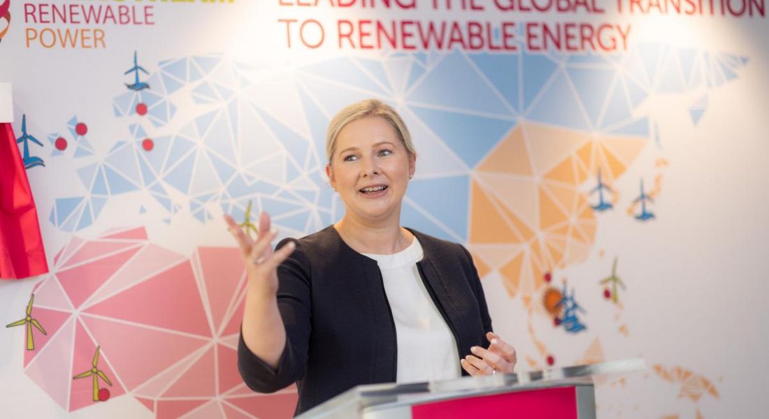 A woman speaking on a stage with a coloured map of the world on a wall behind her. She is Mary Quaney, Group CEO of Mainstream Renewable Power.