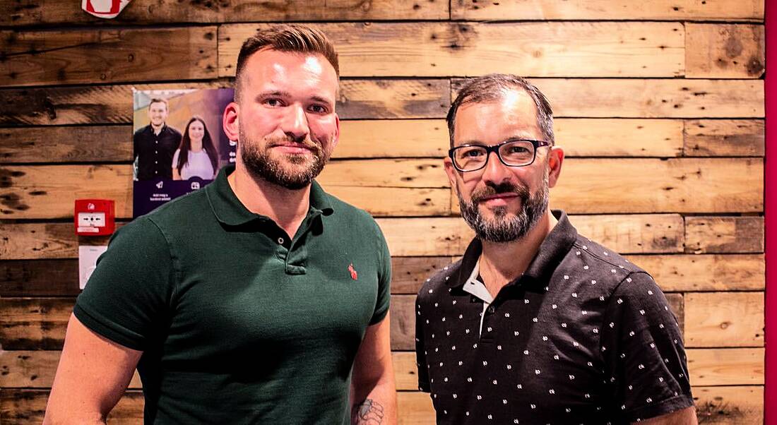 Michal Mysiak and Jozsef Boda standing side by side in a room with wooden planks for walls, celebrating the merger of their European edtech companies.