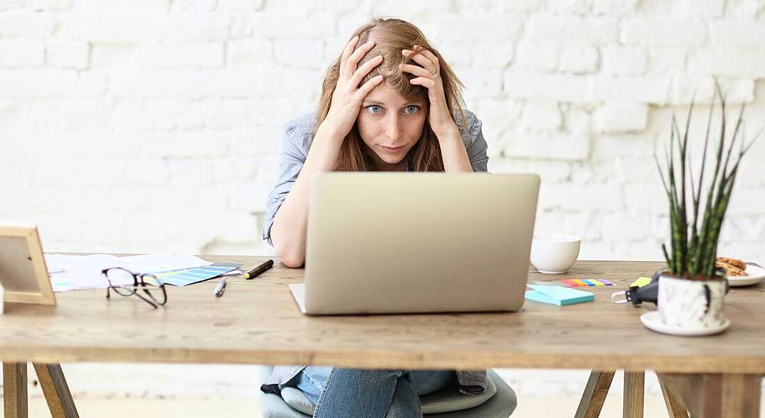 Young woman sitting at a desk with her head in her hands looking at a computer.