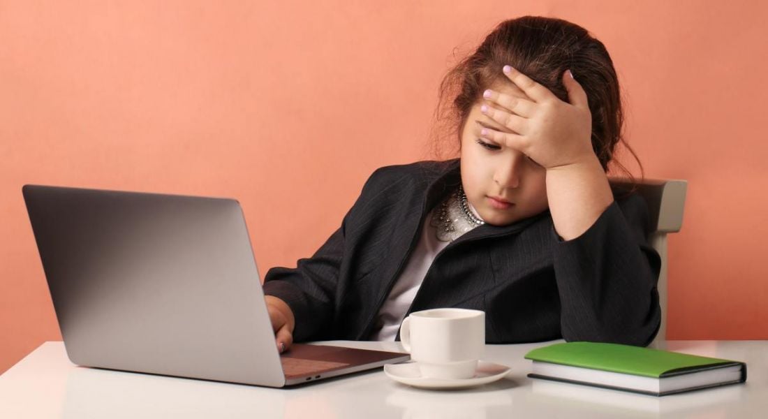 Little girl sitting in front of a computer at a desk with some books and a coffee cup as she's working in tech.