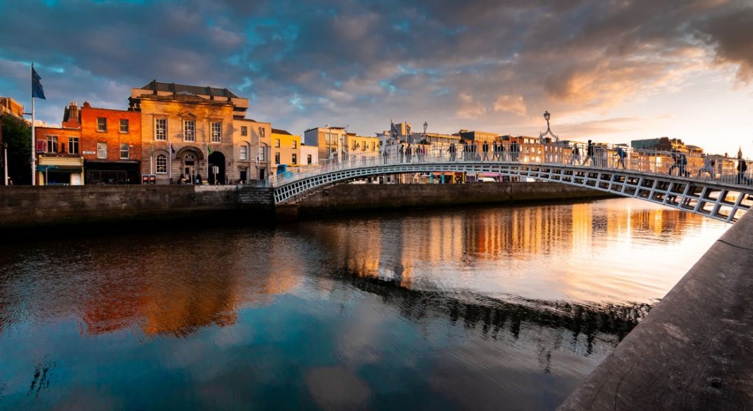 The Ha'penny Bridge over Dublin's River Liffey as the sun sets in the background.