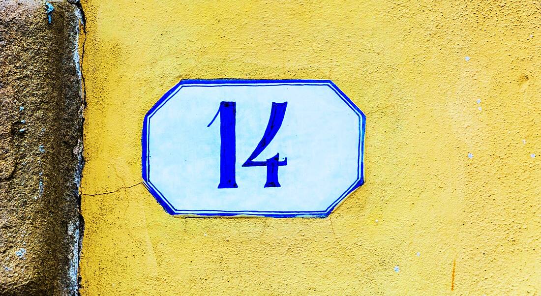 A white and blue tile that says 14 on a yellow wall.