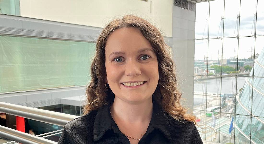 A headshot of a young woman with dark hair. She is wearing a black shirt and standing in PwC’s office building.