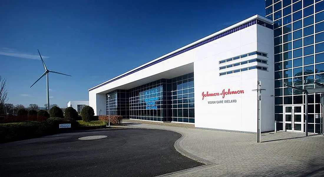 A large manufacturing building with a wind turbine providing energy in the distance.