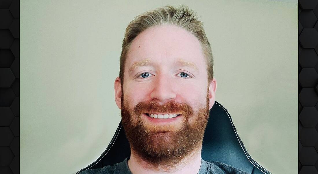 A headshot of a man sitting in an office chair and smiling at the camera.