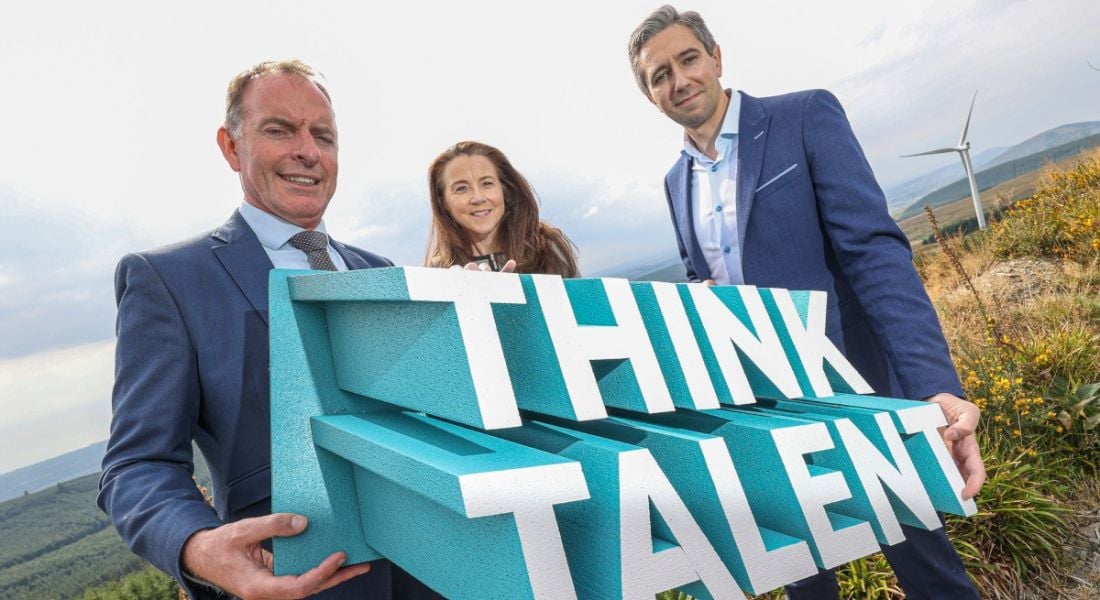 Two men and a woman holding a sign that says think talent. They are standing outdoors.