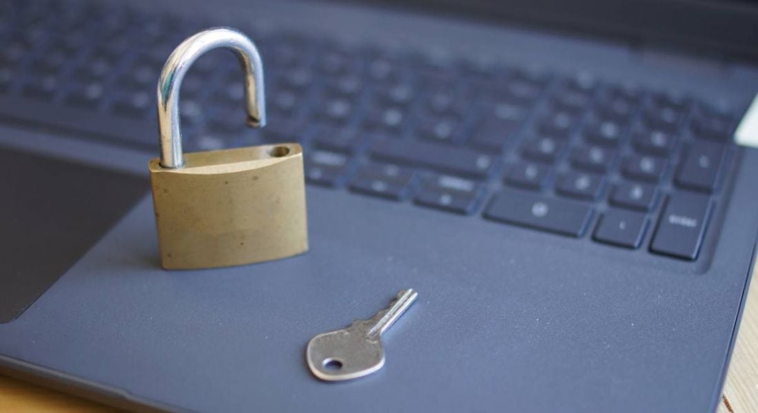 A close-up of an open padlock and a key lying on a grey laptop.