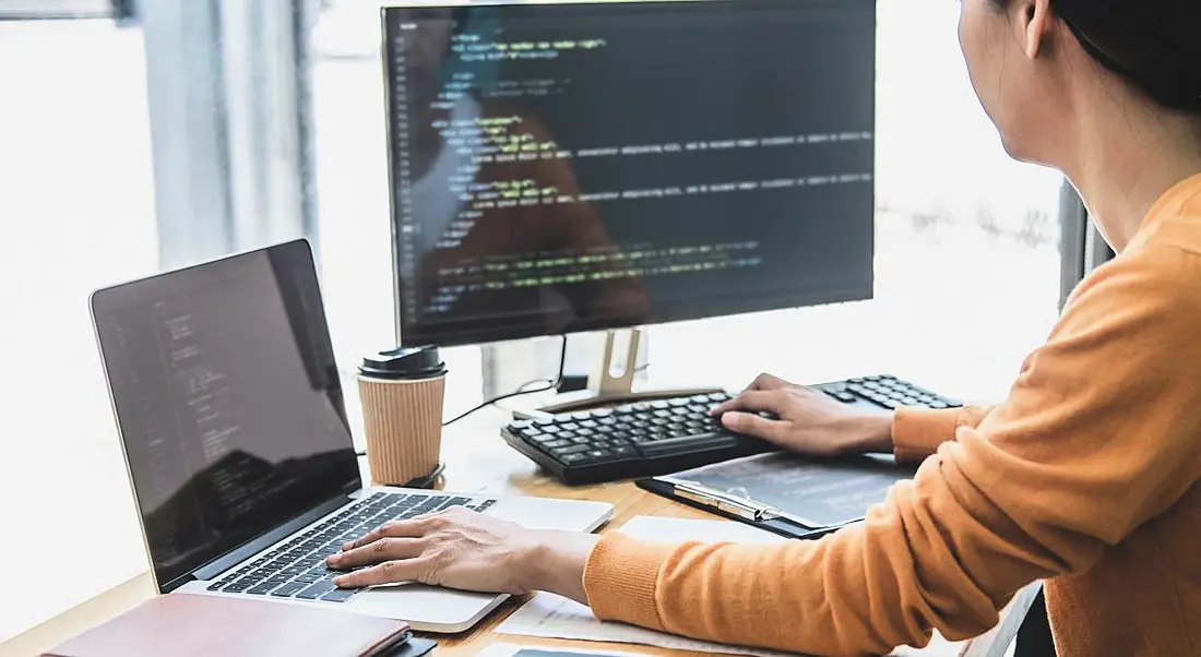 A person sitting at a desk working on two computers with code on them, symbolising the Carbon programming language.