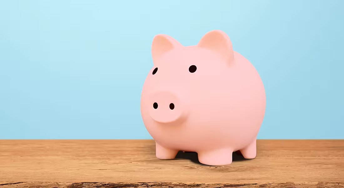 A pink piggy bank sits on a wooden table.