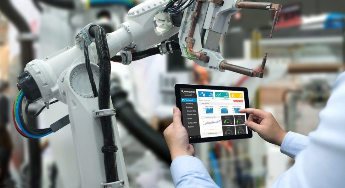 An engineer using a tablet to control a robotic arm involved in automation work, inside a factory.