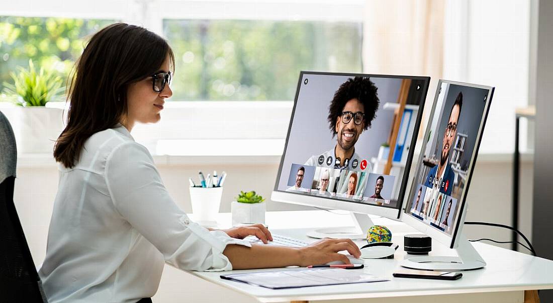 Woman remote working on a computer speaking to other people visible on monitor screens.