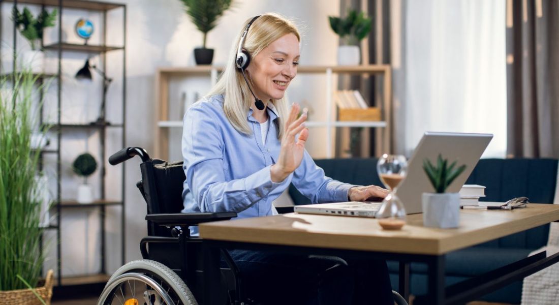 Woman wearing headset and using wheelchair in her office remote working in front of a laptop.