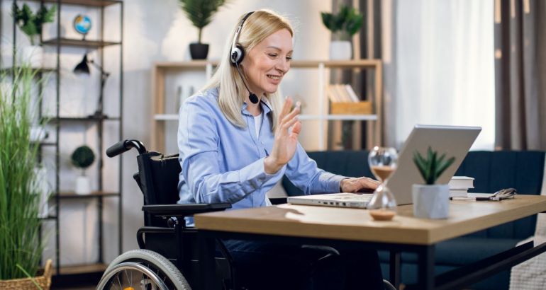 Woman wearing headset and using wheelchair in her office remote working in front of a laptop.