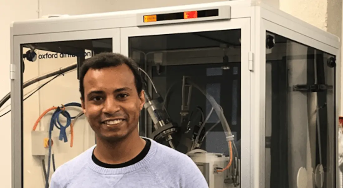 A man stands in a lab in front of a piece of scientific equipment.