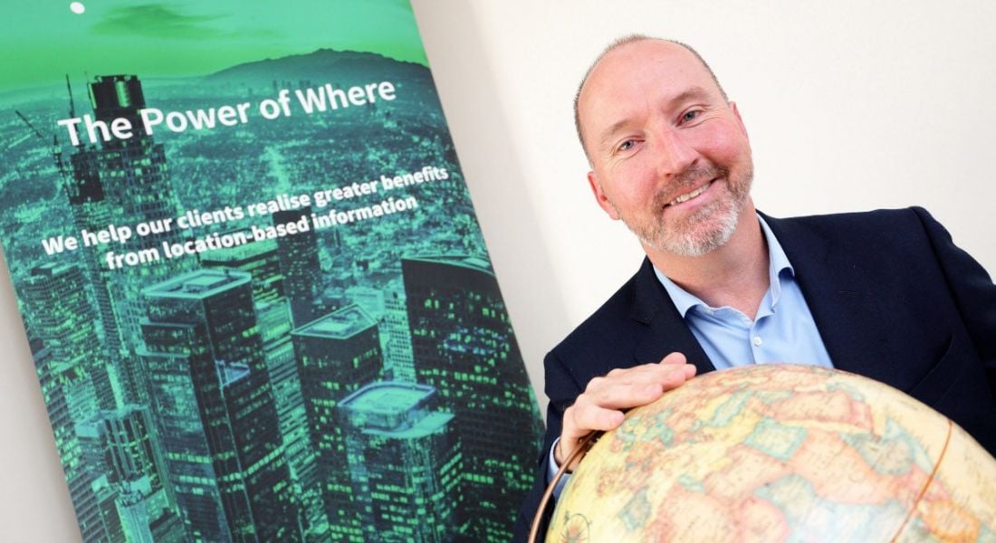 Gamma CEO Feargal O'Neill holding a globe with Gamma poster in the background.