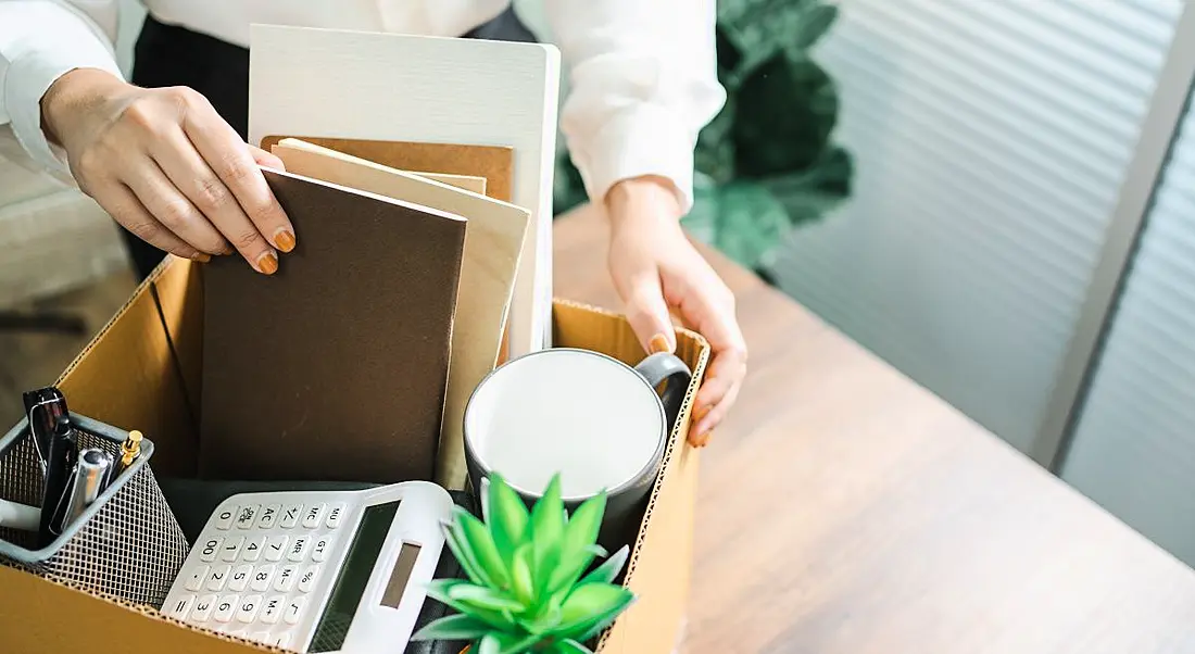 A woman packing a variety of office supplies into a cardboard box to symbolise handing in your notice.