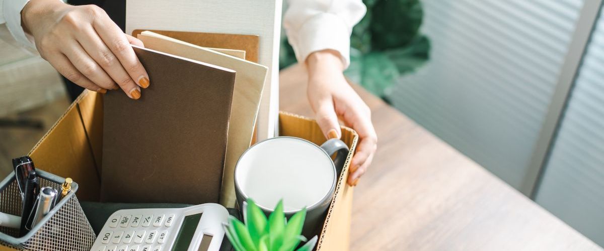 A woman packing a variety of office supplies into a cardboard box to symbolise handing in your notice.