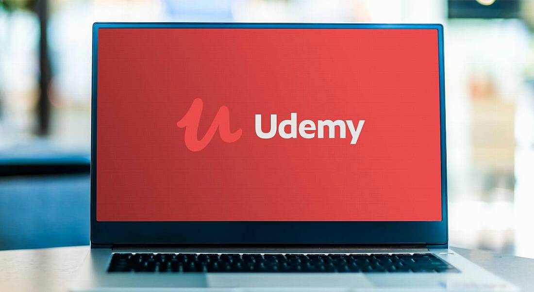 Udemy logo on a red screen on a laptop placed on a table.