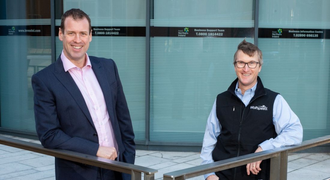 Steve Harper and David Costar of Invest Northern Ireland and Wolfspeed standing leaning against a railing outside a glass-fronted building.