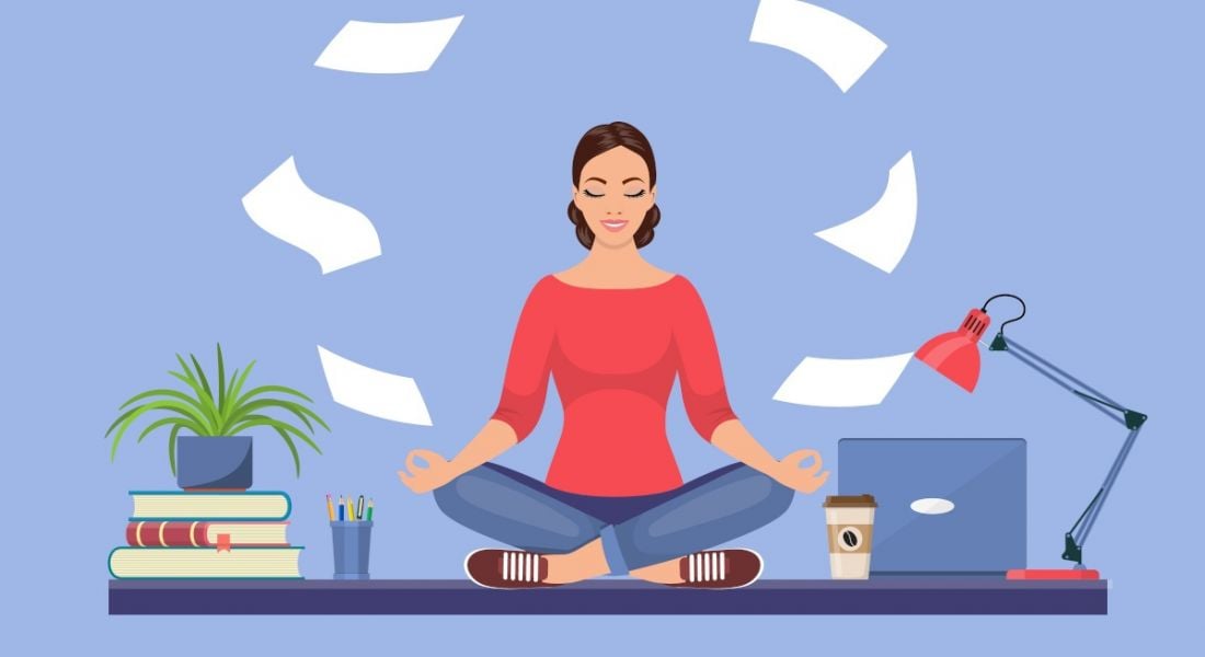 A vector image of a woman sitting cross-legged on a desk with books and a laptop on it. She is practising yoga while several pieces of paper float around her head to symbolise wellbeing.