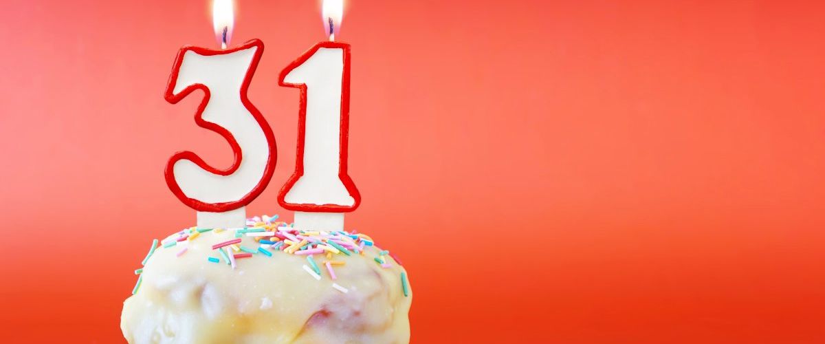 Number candles that say 31 sit on a small iced cake against a red background.