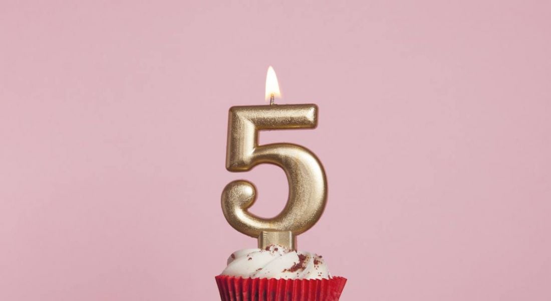 Number five gold candle sitting on a cupcake against a pale pink background.