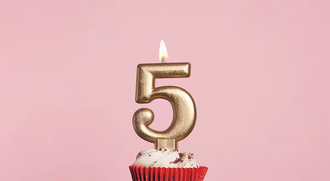 Number five gold candle sitting on a cupcake against a pale pink background.