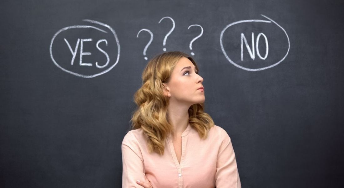 Evaluating a job offer: Woman standing in front of a blackboard with the words yes and no and question marks written over her head. She looks uncertain.