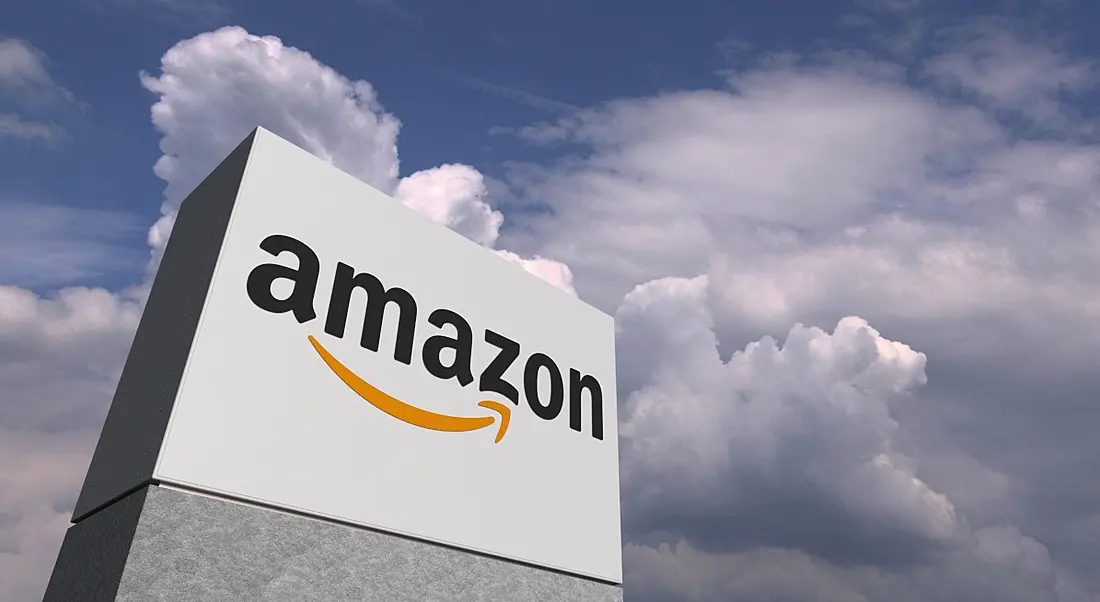 Amazon company logo on a large blocky sign structure stretching into the clouds in a blue sky.