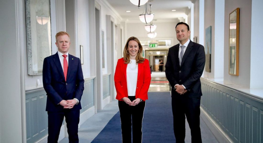 Two men and a women in business attire stand in a corridor of Government buildings in Dublin.