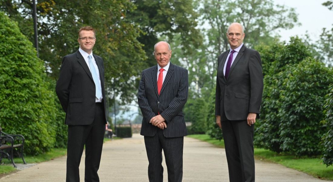 Three men in suits from Regtick standing in a line outside in a tree-lined avenue.