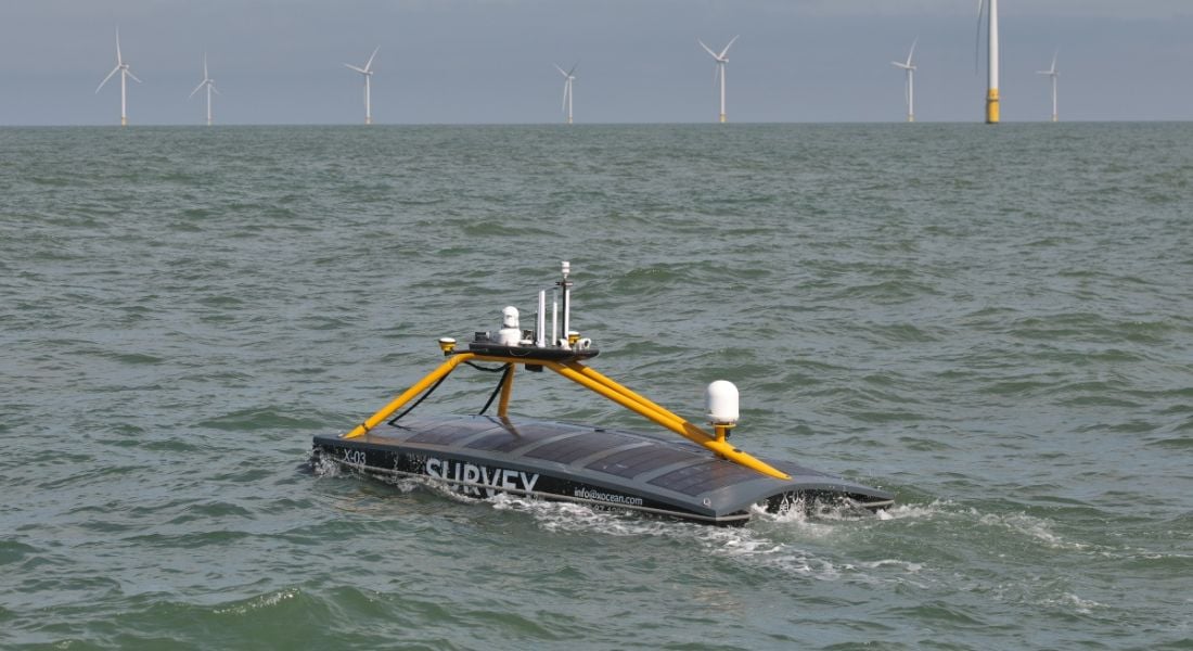 An Xocean unmanned surface vehicle with wind farms in the background.
